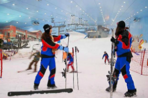 Two women in ski gears are standing in a snowy area, surrounded by fellow skiers in the background. 