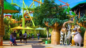 A diverse group of visitors and families walk through a large, rustic timber gateway framed by lush subtropical gardens and tall Eucalyptus trees. Informative conservation signage featuring the Dreamworld Wildlife Foundation logo is visible, highlighting the park's global mission to protect endangered species like Tigers and Koalas. 