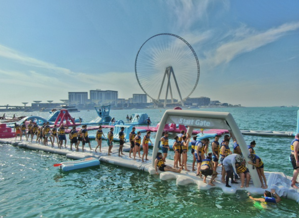 People lined up on an inflatable slide at Aqua Fun Waterpark in Dubai. The giant Ferris wheel can be seen in the background.