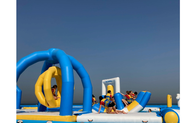 A group of people is seen enjoying their time on an inflatable obstacle course. The course is blue and yellow in color
