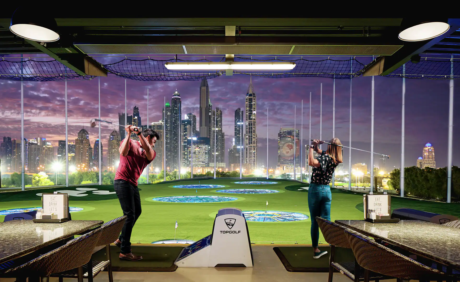 Two people playing indoor golf overlooking Dubai skyline